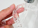 Patient rinsing clear aligner in sink