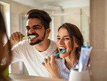 Couple smiling while brushing teeth in bathroom