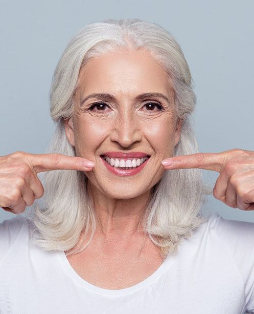 woman with dentures in Denver, CO pointing to her smile 