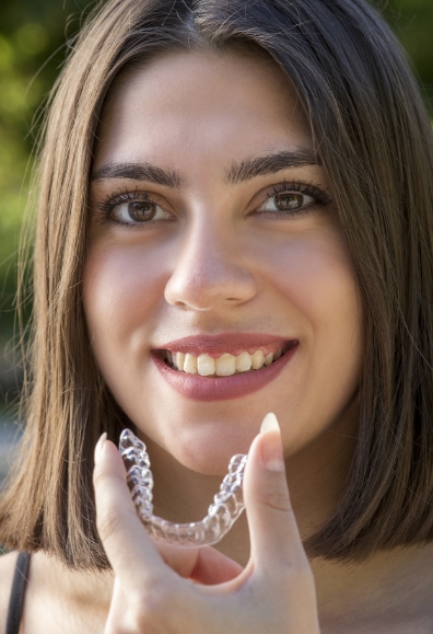 Smiling woman placing an Invisalign tray in her mouth