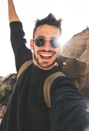 Man smiling with mouth open and arms raised on sunny day with mountain in background