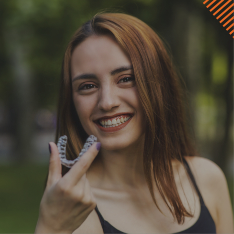 Smiling young woman holding Invisalign clear aligner