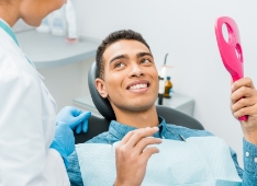 Man in a dental chair looking at the dentist while holding a mirror