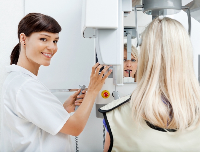 Dental team member capturing 3 D C T cone beam images of woman's smile