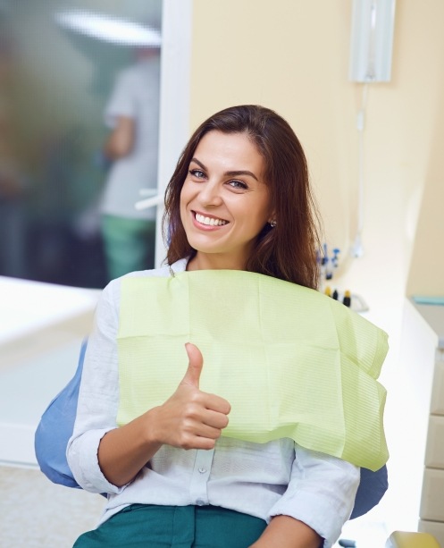 Woman in dental chair giving a thumbs up after receiving dental services