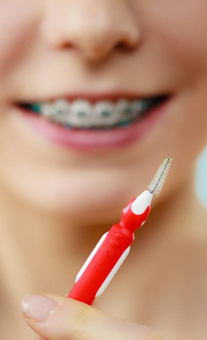 girl with traditional braces in Denver holding dental tools