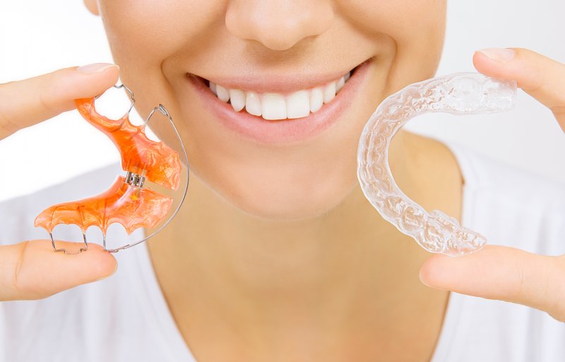 Woman holding both a traditional and plastic retainer.